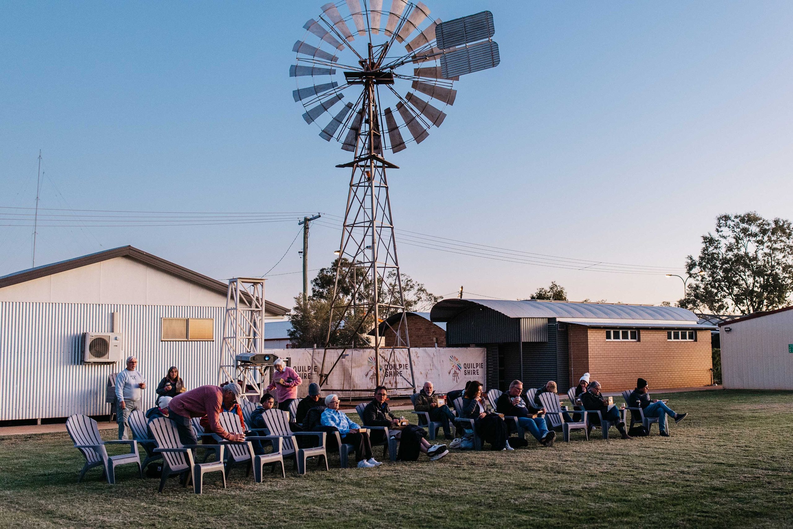 people sitting in lawn chairs with large windmill behind them